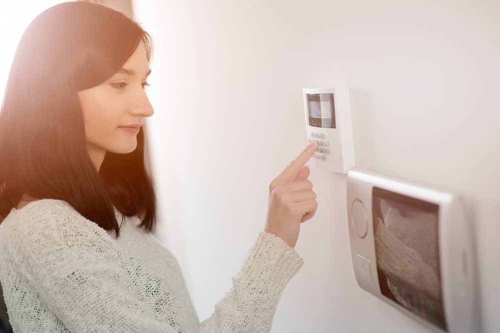 Young Brunette Woman Entering Code On Keypad Of Home Security