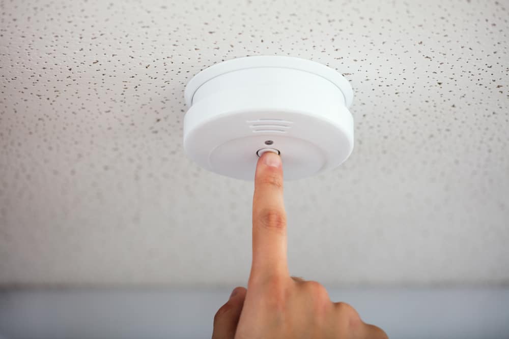 person pressing smoke alarm button with finger.