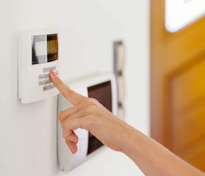 Young Woman Entering Authorization Code Pin On Home Alarm Keypad.